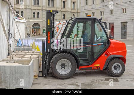 Trieste, Italie - 08 octobre 2024 : chariot élévateur rouge Manitou soulevant des poids en béton pour la tente Pop Up Canopy à City Square. Banque D'Images