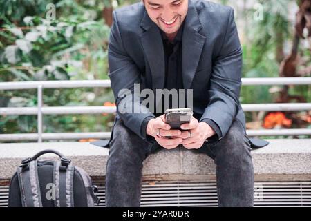 détail des mains d'un homme latino utilisant son téléphone intelligent en souriant Banque D'Images