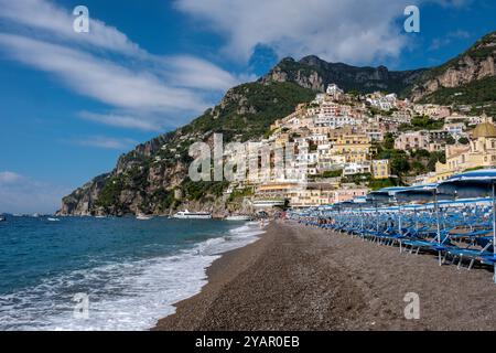 Nichée sur la côte amalfitaine, la ville pittoresque de Positano présente des bâtiments colorés descendant les falaises, avec des chaises de plage de sable bordant t Banque D'Images