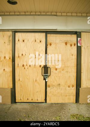 Portes doubles verrouillées recouvertes de contreplaqué d'un magasin et fenêtres latérales vue rapprochée. Horizontal avec espace pour la copie. Sécurisez-les pour éviter les dommages causés par la tempête Banque D'Images