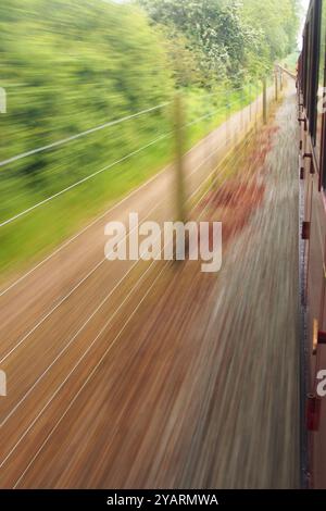 Une vue donnant par la fenêtre d'un carraige de chemin de fer mobile et à voie étroite sur le chemin de fer de Bure Valley, Norfolk, Angleterre, Royaume-Uni Banque D'Images