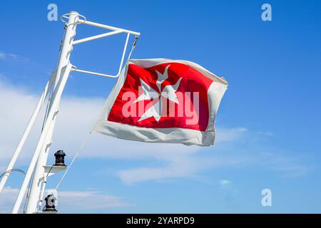 Drapeau maltais sur la poupe d'un navire de croisière sur fond de ciel bleu, rouge, bordé de blanc et chargé d'une croix maltaise blanche Banque D'Images