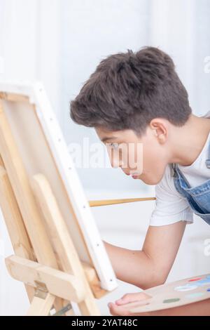 Un adolescent concentré peint une image sur une toile. Il est concentré sur son travail et il s'amuse. La peinture est probablement une représentation de Banque D'Images