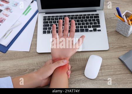 Homme souffrant de douleur au poignet à la table en bois, gros plan. Travail de bureau, syndrome du canal carpien Banque D'Images