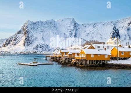 Sakrisoy village de pêcheurs et montagnes enneigées en hiver sur les îles Lofoten, Norvège. Paysage d'hiver avec des maisons traditionnelles de rorbu jaune sur pilotis Banque D'Images