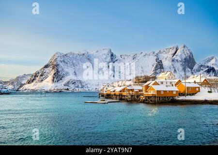 Sakrisoy village de pêcheurs et montagnes enneigées en hiver sur les îles Lofoten, Norvège. Paysage d'hiver avec des maisons traditionnelles de rorbu jaune sur pilotis Banque D'Images