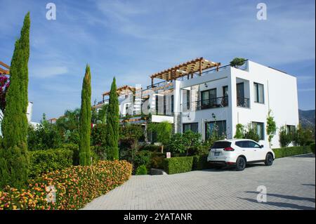 Nichée au milieu d'une verdure vibrante, cette villa élégante présente une architecture élégante, des patios ensoleillés et des fleurs colorées sous un ciel bleu clair. Banque D'Images