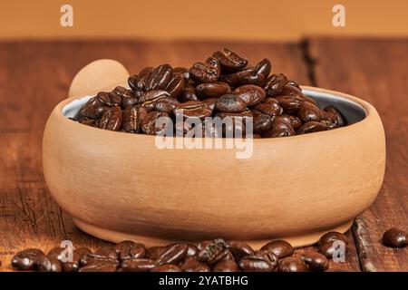 Gros plan de grains de café fraîchement torréfiés dans un récipient en céramique sur une vieille table en bois Banque D'Images
