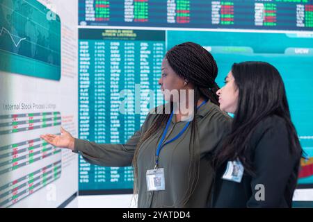 Une équipe diversifiée d'employés examine les infographies sur grand écran pour évaluer l'offre et la demande, les moyens d'augmenter le budget organisationnel et de développer l'entreprise à l'échelle internationale. Banque D'Images