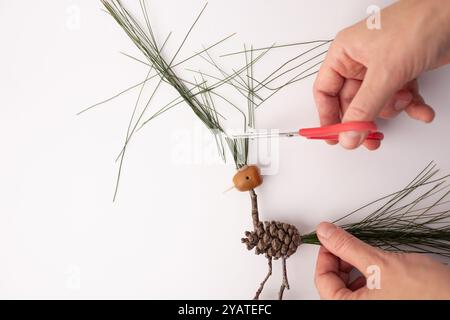 Un oiseau fait à la main fabriqué à partir de pommes de pin et de brindilles, une paire de ciseaux coupant sur le dessus d'une branche de pin, art populaire, figure entière, sur un fond blanc, Banque D'Images