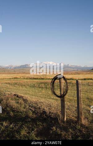 Un rouleau de vieux fils barbelés rouillés pend sur le haut du poteau de clôture. Le fil jeté de la réparation de clôture est dangereux pour les animaux et l'équipement. Comté de Teton, Montana. Banque D'Images