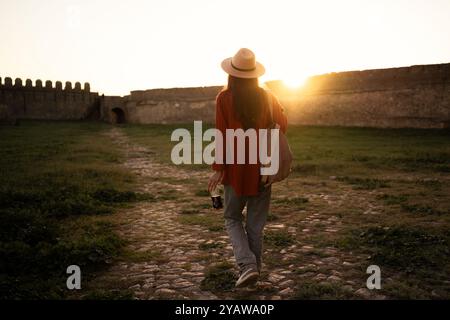 vue arrière touriste avec sac à dos marchant autour du territoire de la forteresse, voyageuse visitant le vieux château au coucher du soleil dans la soirée. Copier l'espace Banque D'Images