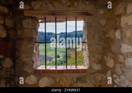 Une fenêtre barrée dans un mur de pierre encadre une vue paisible sur les collines verdoyantes, les champs et les forêts lointaines pendant la journée Banque D'Images