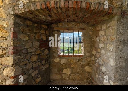 Une fenêtre barrée dans un mur de pierre encadre une vue paisible sur les collines verdoyantes, les champs et les forêts lointaines pendant la journée Banque D'Images