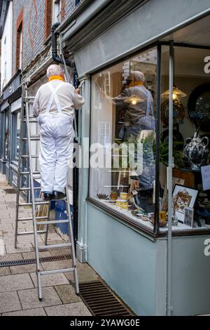 Un homme senior peignant et décorant Un magasin extérieur, High Street, Lewes, East Sussex, Royaume-Uni. Banque D'Images