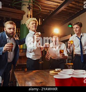 Amis proches habillés tenue de bureau jouer au bière-pong, rire et avoir un grand temps avec des boissons à table. Banque D'Images