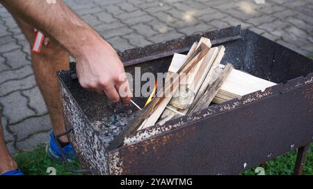 Une main Mans utilise des allumettes pour allumer un feu dans un gril pour barbecue. Démarrage du feu pour griller dans la cour arrière. Banque D'Images