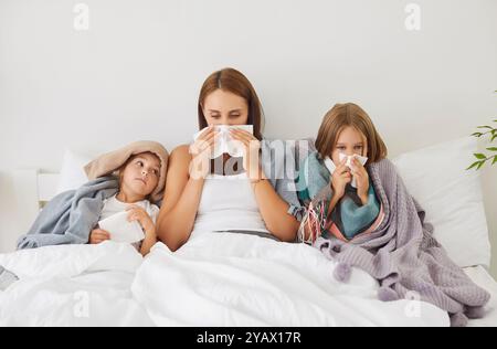 Jeune famille malade de mère et d'enfants couchés dans le lit couverts de couvertures avec grippe saisonnière ou rhume Banque D'Images