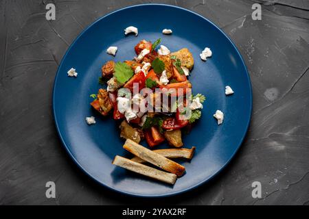 Salade avec aubergines caramélisées, coriandre, tomates et fromage à la crème sur une assiette bleue avec du pain grillé sur fond gris. Photo de haute qualité Banque D'Images