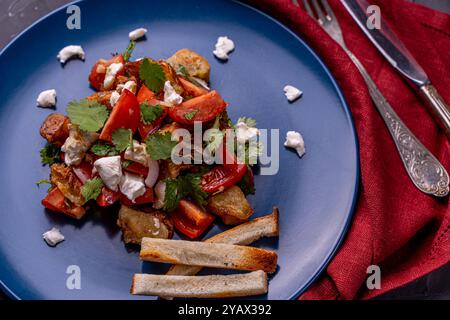 Salade avec aubergines caramélisées, coriandre, tomates et fromage à la crème sur une assiette bleue avec du pain grillé sur fond gris. Photo de haute qualité Banque D'Images