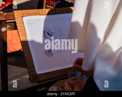 gros plan d'une femme par derrière brodant une fleur sur une toile blanche encadrée Banque D'Images