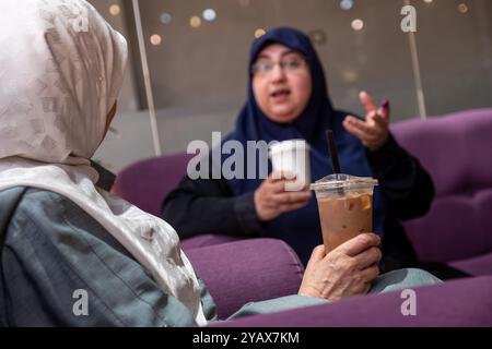 Deux femmes portant des hijabs sont engagées dans une conversation amicale autour d'un café dans un cadre intérieur confortable. La scène reflète la chaleur, l'amitié et le cultu Banque D'Images