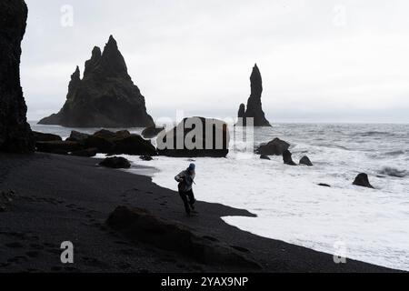 Un homme s'enfuit d'une vague sur une plage de sable noir en Islande Banque D'Images