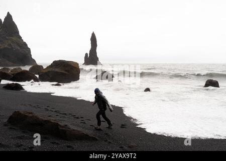 Un homme s'enfuit d'une vague sur une plage de sable noir en Islande Banque D'Images