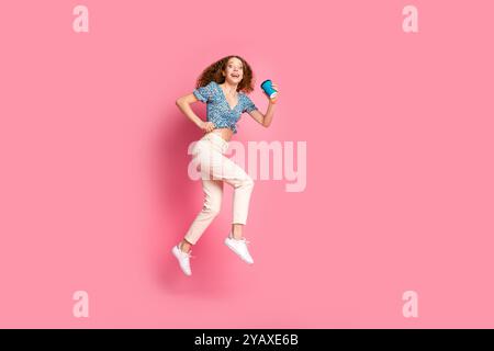 Femme joyeuse sautant avec du café sur fond rose Banque D'Images