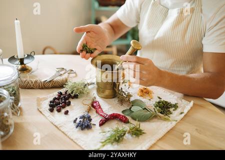Vue de côté de l'homme ajoute de la menthe séchée à un mortier et pilon. Suppléments sains et nutritionnels faits maison Banque D'Images