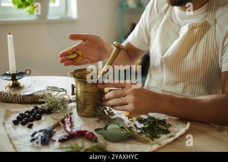 Vue de côté de l'homme ajoute des pétales de rose séchés à un mortier et un pilon. Suppléments sains et nutritionnels faits maison Banque D'Images