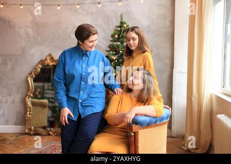 Trois femmes se sont joyeusement rassemblées autour d'un sapin de Noël magnifiquement orné. Entouré de lumières scintillantes et de décorations festives. Ce moment capture l'essence de la cohésion de la famille pendant Noël, mettant en valeur la joie et la célébration qui accompagnent le partage de moments spéciaux ensemble Banque D'Images