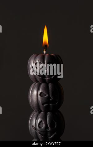 Bougie de citrouille noire brûlant brillamment sur fond sombre, créant une atmosphère effrayante Banque D'Images