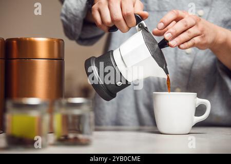 Verser le café frais du Moka pot dans la tasse blanche sur le comptoir de cuisine Banque D'Images