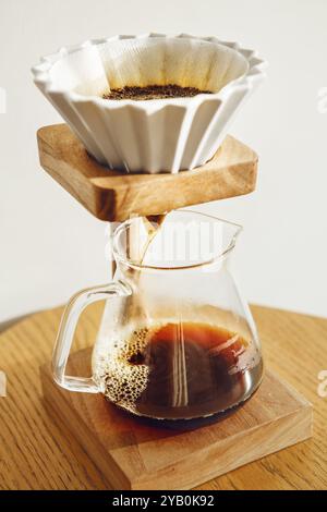 Gros plan du café en cours de préparation à l'aide d'une méthode alternative avec entonnoir de type Origami et support à partir duquel la boisson coule dans un pot en verre transparent Banque D'Images