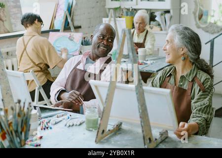 Plan à angle élevé de couple senior biracial discutant belle tout en assistant à la thérapie artistique ensemble dans un studio de dessin spacieux moderne Banque D'Images