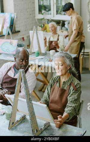 Plan vertical à grand angle d'un mari afro-américain regardant sa femme caucasienne avec amour alors qu'elle peignait sur toile Banque D'Images