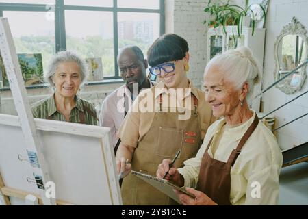 Plan en grand angle d'artistes féminines seniors souriant tandis que son jeune professeur adulte et ses amis biraciaux regardaient sa peinture Banque D'Images