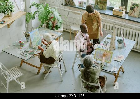 Prise de vue en grand angle d'élèves seniors concentrés sur la peinture tandis que le jeune professeur adulte vérifiait les progrès Banque D'Images
