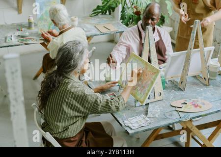 Plan à angle élevé de femme senior méconnaissable dessinant des nuages sur toile avec des peintures aquarelles dans un studio de dessin pendant la thérapie artistique Banque D'Images