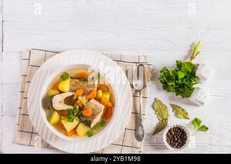 Soupe claire de brochet avec légumes, persil et épices dans un bol blanc sur une table en bois blanc avec cuillère, feuilles de laurier et grains de poivre, vue horizontale de A. Banque D'Images