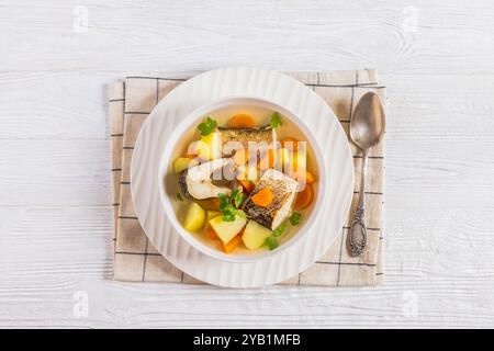 Soupe claire de brochet du Nord avec légumes, persil et épices dans un bol blanc sur une table en bois blanc avec cuillère, vue horizontale d'en haut, gros plan, fla Banque D'Images