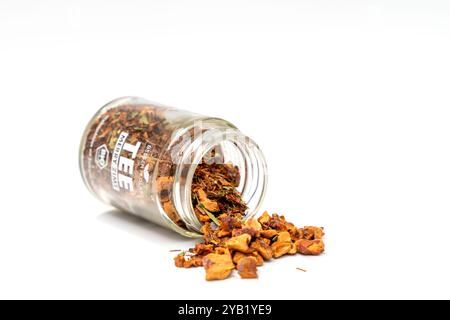 Une canette de thé de pomme à la cannelle de Noël est ouverte et son contenu est dispersé sur un fond blanc. Le pot est à moitié vide et le thé est brun. Banque D'Images