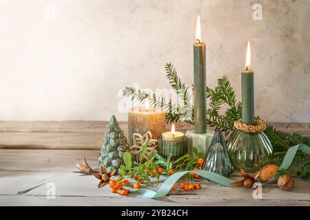 Décoration naturelle de l'Avent et de Noël avec quatre bougies différentes, branches, baies, noix et plus sur des planches de bois rustiques contre un plâtre beige Banque D'Images