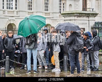 Un groupe d'adolescents se tient devant les bureaux de l'université Old Schools à Cambridge, en Angleterre, un jour de pluie. Banque D'Images