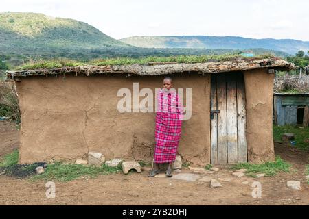 Jeune garçon Masai debout devant une maison traditionnelle Masai faite de bouse de vache, boue et branches de bois, Masai Mara, Kenya, Afrique Banque D'Images