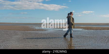 Femme dans des bottes wellington marchant sur la plage à marée basse Banque D'Images