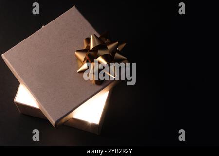 Boîte cadeau avec ruban doré et lumière incandescente sur fond sombre Banque D'Images