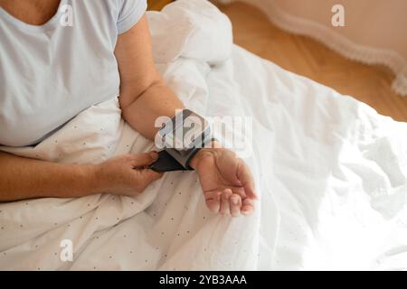 Gros plan de la femme vérifie sa tension artérielle, un tonomètre est porté sur son poignet dans un lit. Dispositif médical de mesure de la pression artérielle et de la fréquence cardiaque Banque D'Images