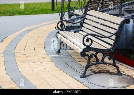 Un banc de parc en bois magnifiquement conçu est situé sur une passerelle en briques légèrement incurvée entourée de verdure et de paysages luxuriants Banque D'Images